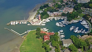 An aerial view of a marina with boats docked, a lighthouse, and surrounding residential buildings. - Muirfield RANCH/ On #2 Golf Links / Pool / Walk to HARBOUR TOWN/ 4 Bikes / Pet (Hilton Head Island)