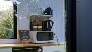 A kitchen counter with a white microwave, a coffee maker, and a shelf with glassware and a blue bottle. A sign reads "Welcome to Ryan's Ranch Norman & Boone." - Ryans Ranch by Tiny Away (Belgrove)