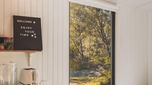 A bedroom with a large window, a bed, a laptop, and a coffee maker. - Mirror Reflections 1 by Tiny Away (Tamborine)