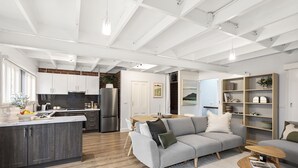 A modern kitchen with white cabinetry, a central island, and a dining area with a grey sofa and wooden side tables. - Cottage haven close to Ascot Vale cafes, restaurants, racecourse and showgrounds (Ascot Vale)