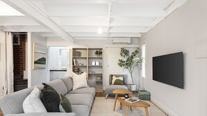 A modern living room with a grey sofa, a wooden coffee table, a bookshelf, and a TV mounted on the wall. - Cottage haven close to Ascot Vale cafes, restaurants, racecourse and showgrounds (Ascot Vale)