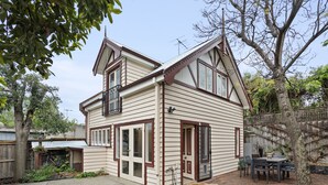A two-story house with a front porch, a dining area with a table and chairs, and a garage. - Cottage haven close to Ascot Vale cafes, restaurants, racecourse and showgrounds (Ascot Vale)