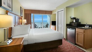 A hotel room with a bed, bedside lamps, a small desk, a kitchen area with a refrigerator, and a balcony with a view. - Shoreline Serenity: King Bed, Private Balcony (Myrtle Beach)