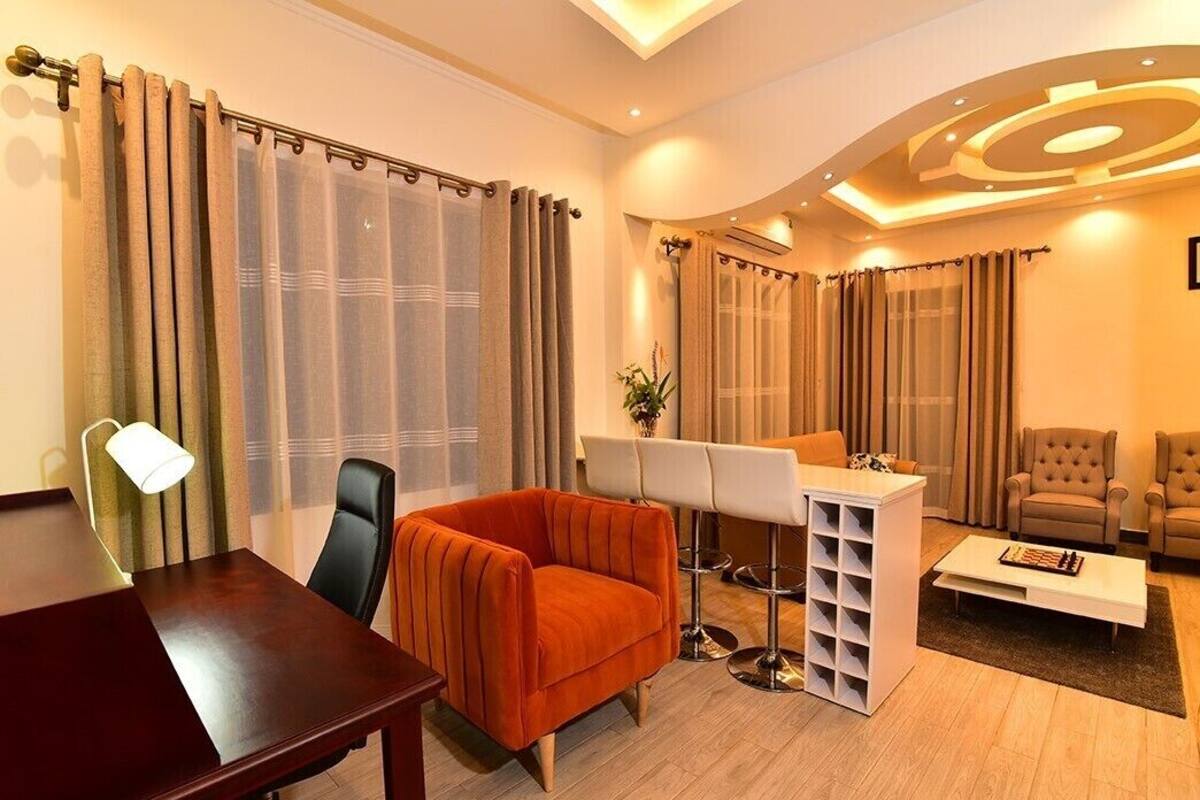 A modern living room with a wooden table, an orange armchair, a white desk with a music stand, and a sofa.