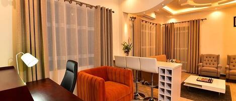 A modern living room with a wooden table, an orange armchair, a white desk with a music stand, and a sofa.