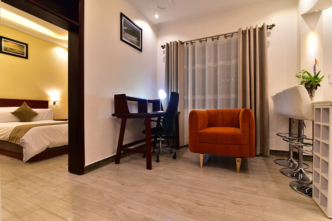 Ein Hotelzimmer mit einem Bett, einem Schreibtisch mit Stuhl, einem orangefarbenen Sessel, einer Lampe und einem Vorhang.