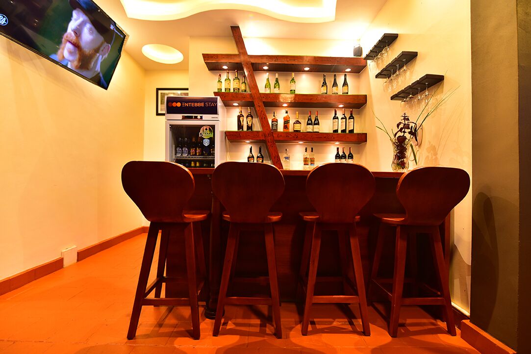 A bar area with wooden chairs, shelves of bottles, and a TV mounted on the wall.