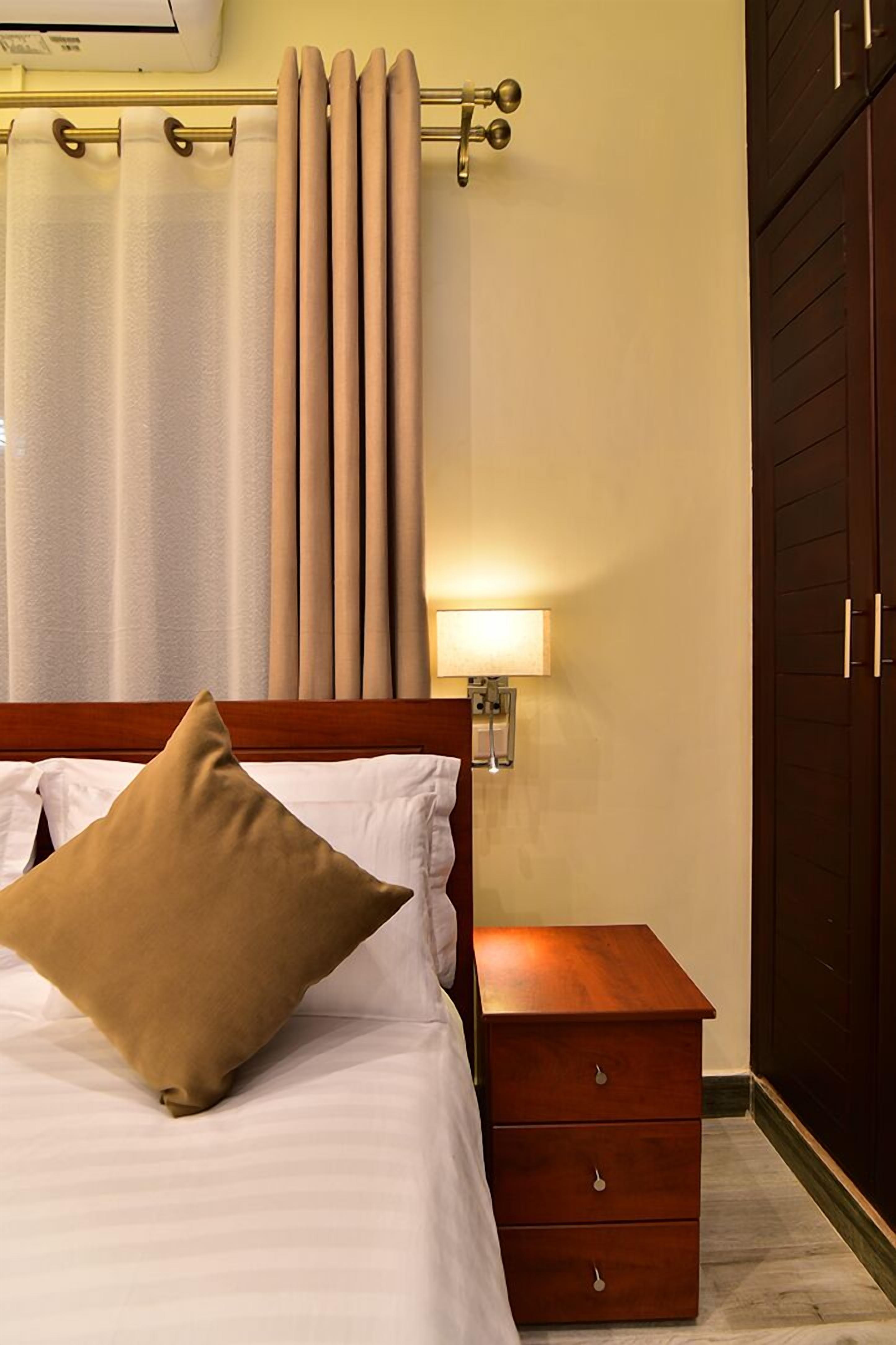 A hotel room with a bed, a nightstand, a lamp, a wardrobe, and curtains.