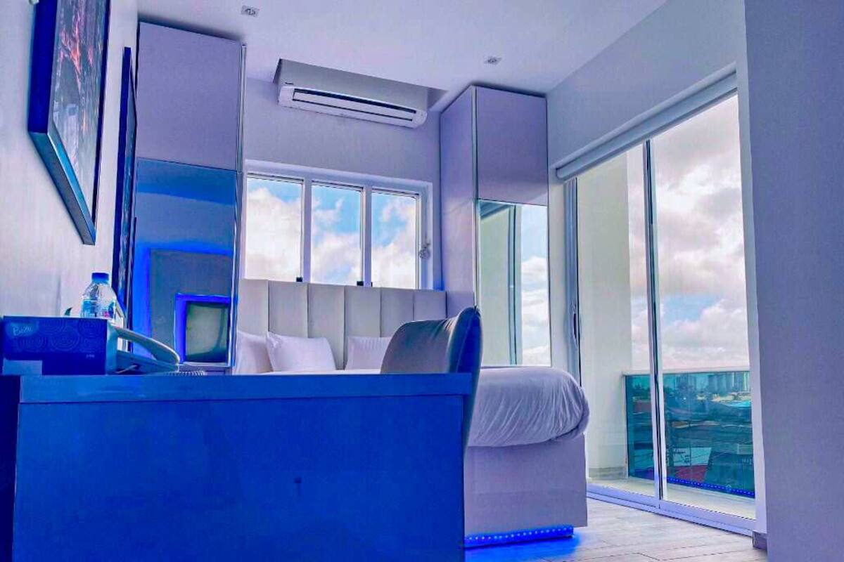 A modern bedroom with a bed, a desk, and a large window.