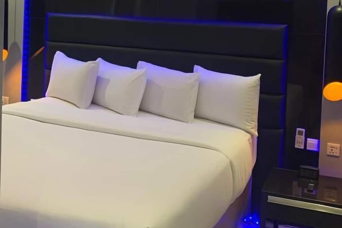 A modern bedroom with a large bed, a dark headboard, and blue ambient lighting.