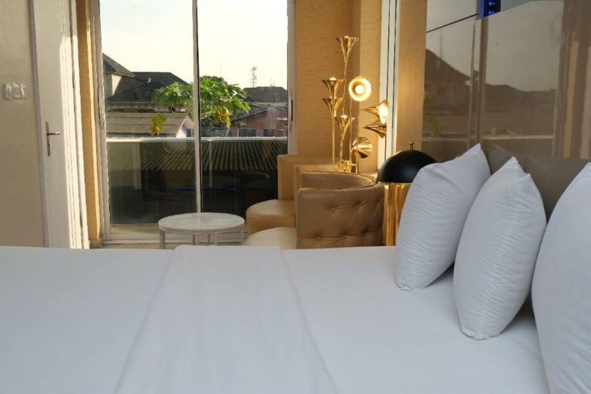 A hotel room with a large bed, a small round table, a sofa, and a view of the outside through a sliding door.