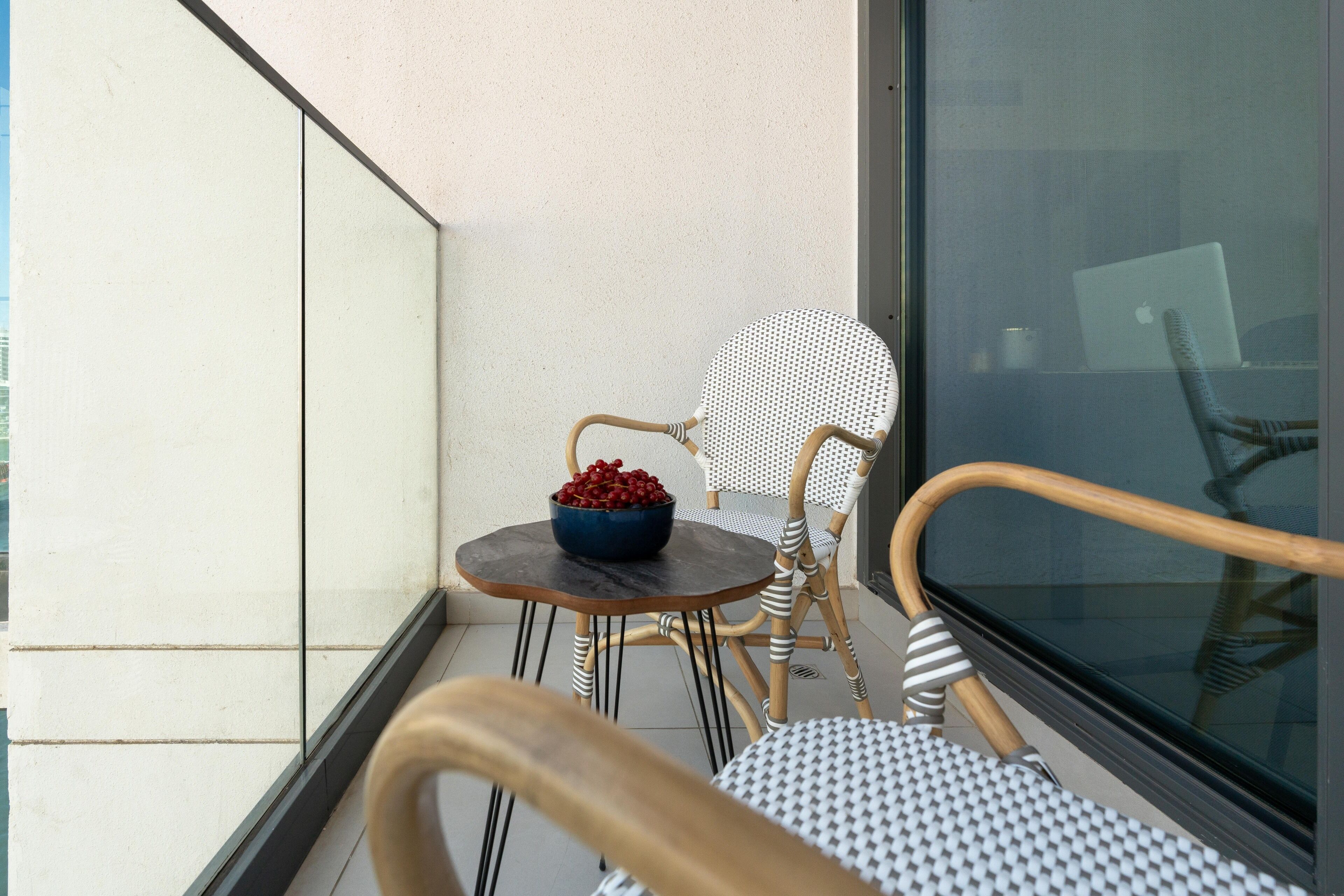 A balcony with wicker chairs, a small round table with a bowl of fruit, and a large window.