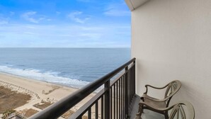 A balcony with a view of the ocean, a chair, and a railing.