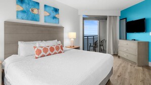 A hotel room with a large bed, a TV, a desk with a lamp, and a balcony with a view. - Newly Renovated Ocean View 3 Bdrm Condo 5th Flr (Myrtle Beach)