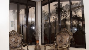 Una habitación con dos sillones decorados, una mesa con cubierta de vidrio y un amplio ventanal con vistas a palmeras.