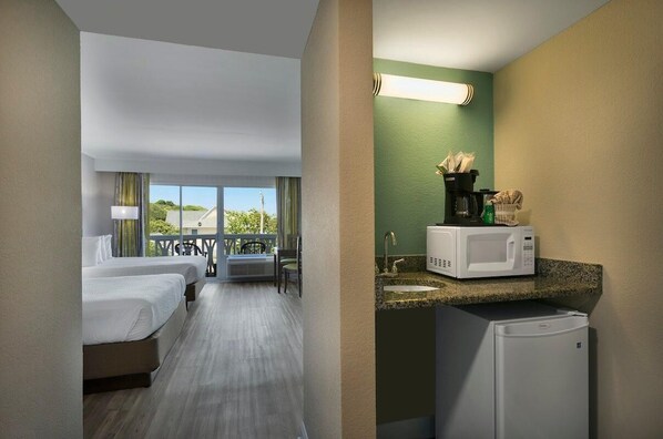 Une chambre d’hôtel avec deux lits, un balcon, une kitchenette équipée d’un four à micro-ondes et d’un réfrigérateur.