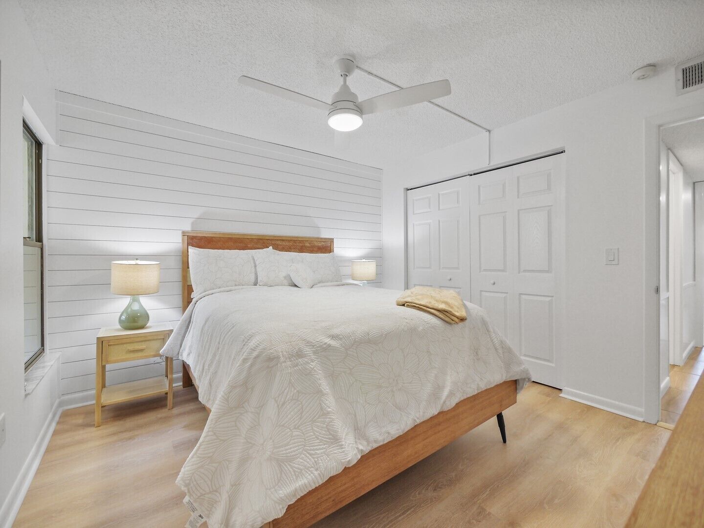 Une chambre à coucher avec un lit en bois, des murs blancs, un ventilateur de plafond et une table de chevet avec une lampe.