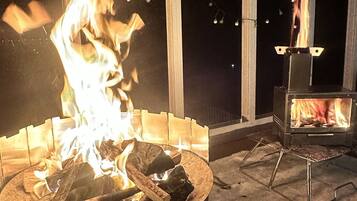 An outdoor fire pit with burning wood, surrounded by a metal grill and a metal table.