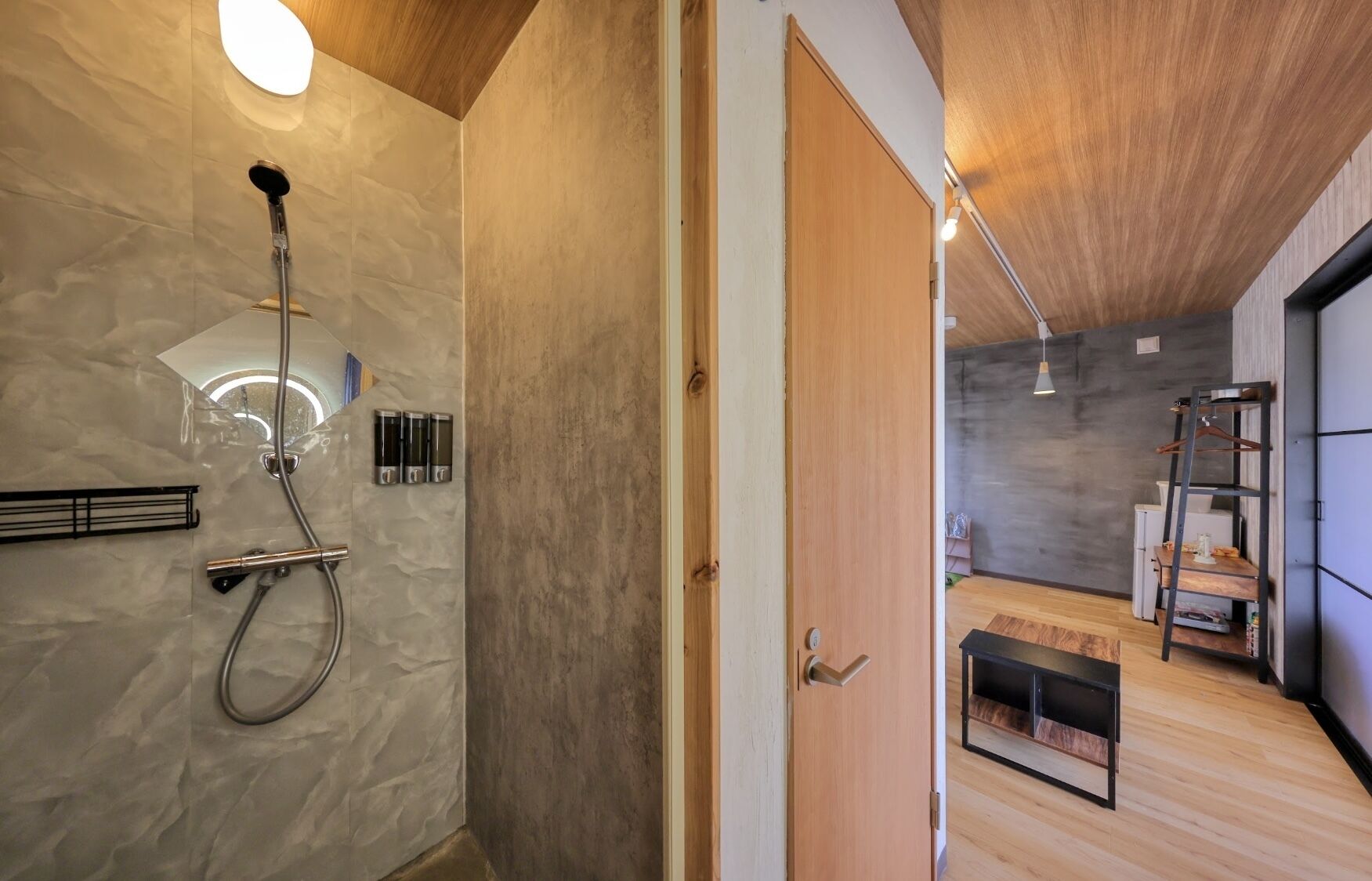 Un baño moderno con ducha, toallero y una puerta de madera que da a una zona de estar con un banco y una escalera.