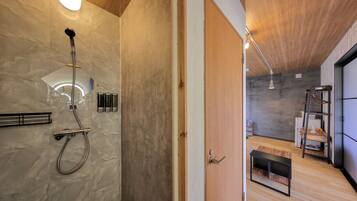 Un baño moderno con ducha, toallero y una puerta de madera que da a una zona de estar con un banco y una escalera.