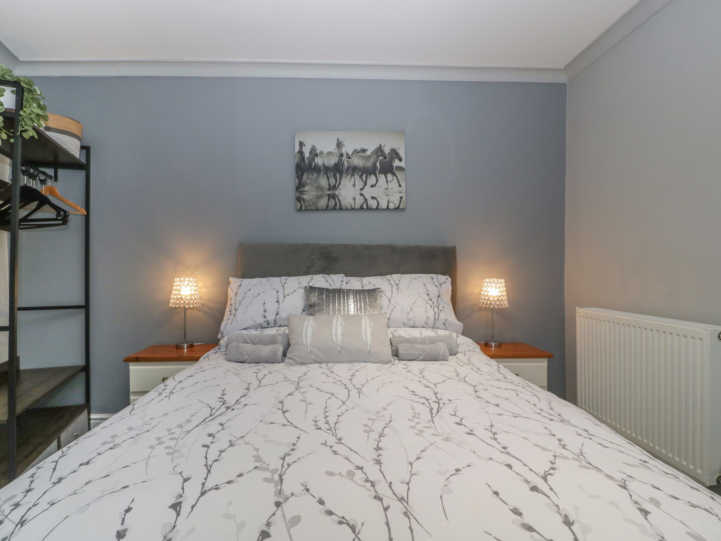 A bedroom with a bed, two bedside lamps, a headboard, a wall-mounted painting, and a radiator.