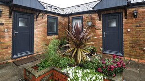 Un bâtiment en briques avec deux portes de couleur foncée et un petit jardin agrémenté de diverses plantes et fleurs.