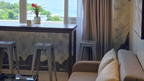 A room with a view of the sea, a sofa, a small table with a potted plant, and two stools. - Stunning and brandnew 1 BR corner unit for 5 Persons - woow ocean-views (Lapu-Lapu City)