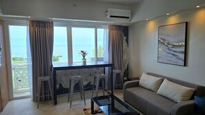A living room with a sofa, a coffee table, and a view of the sea through large windows. - Stunning and brandnew 1 BR corner unit for 5 Persons - woow ocean-views (Lapu-Lapu City)