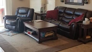 A living room with a ceiling fan, a leather sofa, a coffee table, and a television on the wall. - Private putting green at Johnson Ranch 3 bedroom (San Tan Valley)
