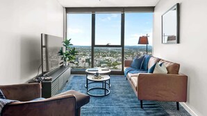 Ein modernes Wohnzimmer mit großem Fenster, einer Couch, einem Couchtisch und einem Fernseher.