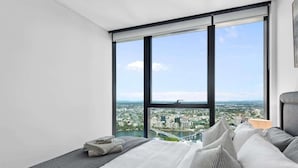 Ein Schlafzimmer mit großem Fenster, einem Bett mit Kissen und Blick auf die Stadt.