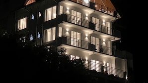 A multi-story building with illuminated windows and balconies, featuring a prominent triangular roof structure.