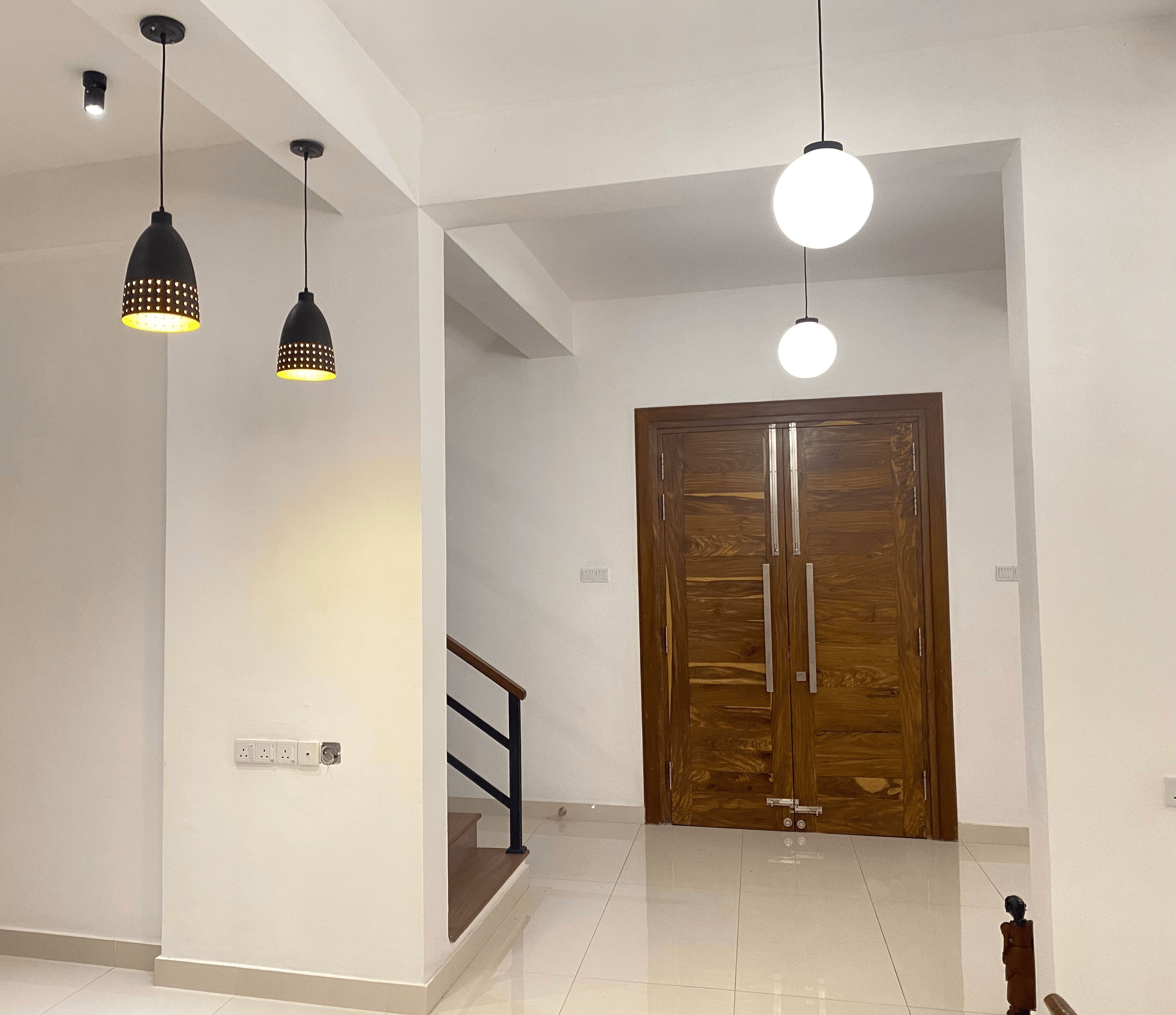A hallway with a wooden door, a staircase, and pendant lighting.