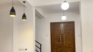 A hallway with a wooden door, a staircase, and pendant lighting.