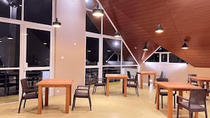 A spacious interior with high ceilings, large windows, and multiple wooden tables and chairs arranged for dining.