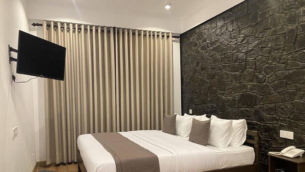 A modern bedroom with a bed, a wall-mounted TV, a stone-textured wall, a small heater, and a bedside phone.