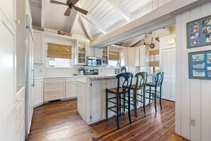 A kitchen with wooden flooring, white cabinetry, a central island, and two bar stools.