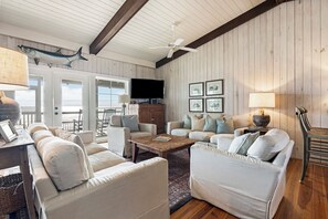 A spacious living room with a large flat-screen TV, white sofas, a wooden coffee table, and a ceiling fan. - Oceanfront Beach House, Sundeck, Gazebo, Boardwalk, Screened Porch with Rockers (Pawleys Island)