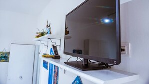 A flat-screen TV mounted on a white wall, with a remote control and decorative items on a shelf below.