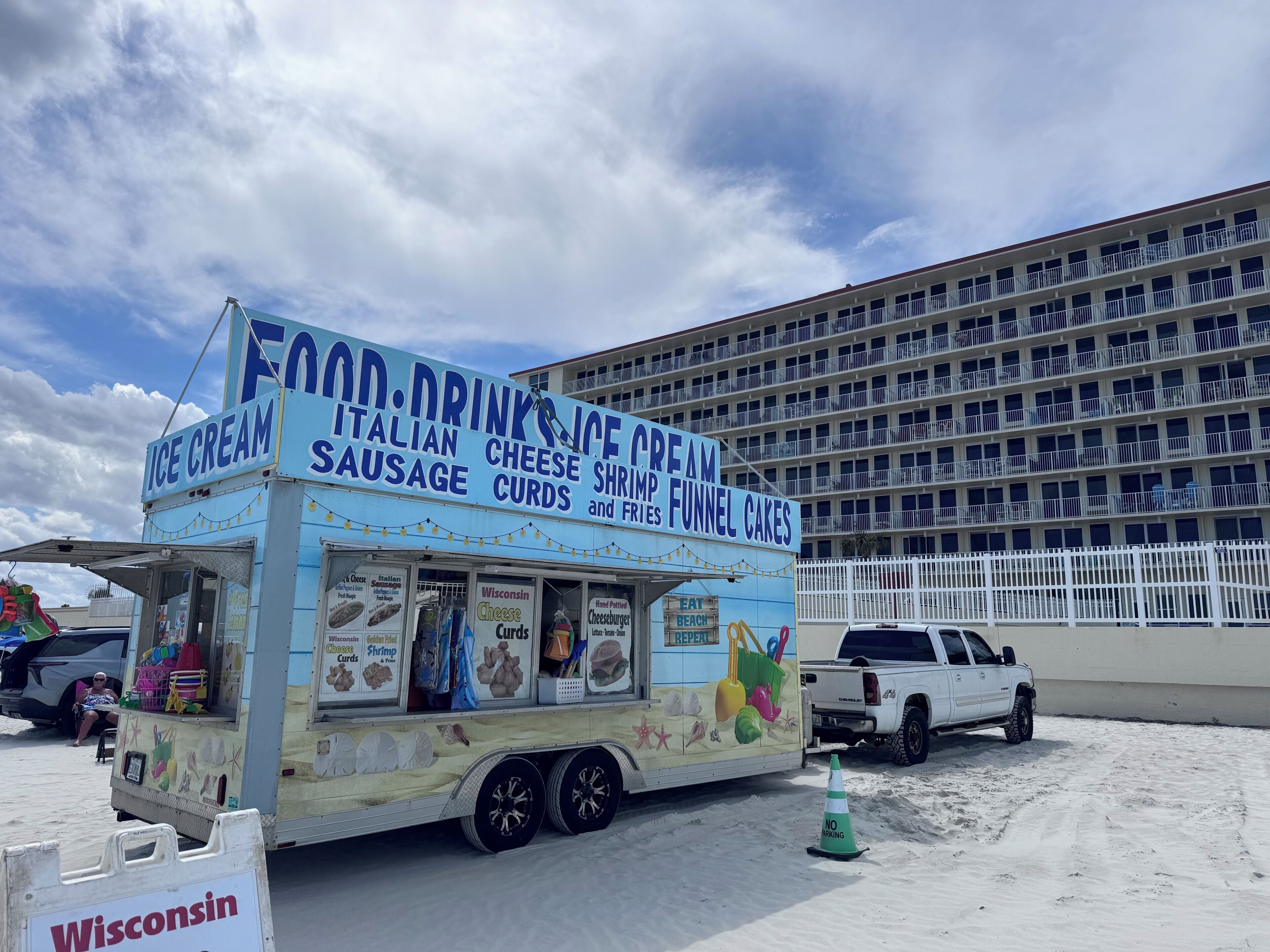 A food truck with a sign advertising ice cream, sausage, cheese, shrimp, and funnel cakes.