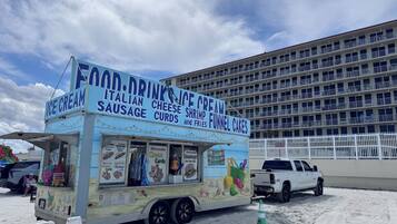 A food truck with a sign advertising ice cream, sausage, cheese, shrimp, and funnel cakes.