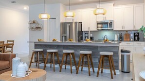 Una cocina moderna con armarios blancos, electrodomésticos de acero inoxidable y una isla central con taburetes.