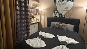 Una camera d'albergo con un letto grande, una testiera, un quadro appeso al muro, una scrivania con una lampada e tende.