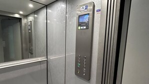 Un ascensore con display digitale e pannello di controllo, pareti metalliche e pavimento riflettente.