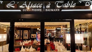 Un ristorante con facciata in vetro, tavoli apparecchiati con tovaglie bianche e sedie rosse, e opere d'arte incorniciate alle pareti.