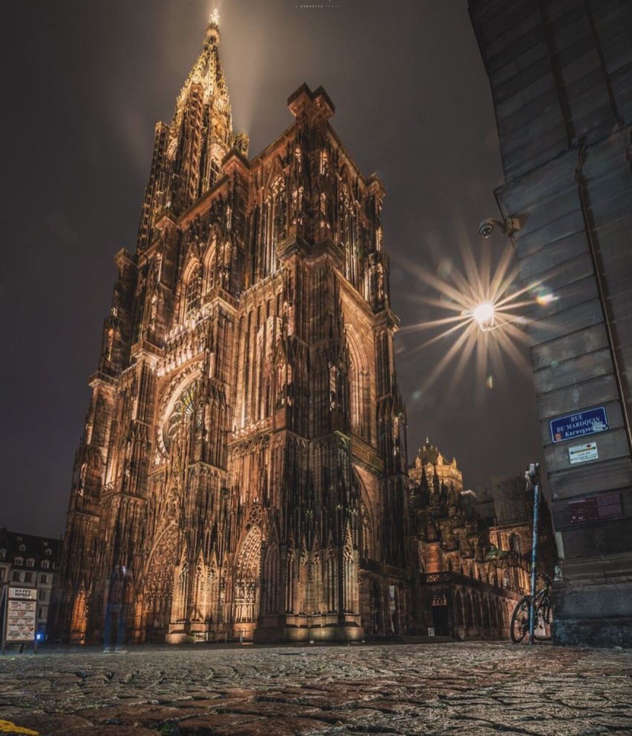 Een gotische kathedraal met ingewikkelde architectuur en een grote klokkentoren, verlicht in de nacht.