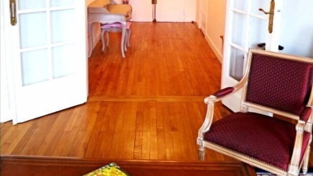 Una habitación amplia con piso de madera, un candelabro y un sillón rojo.