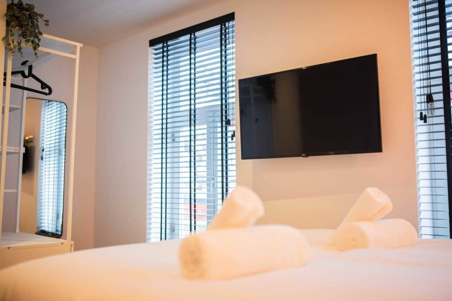 Een hotelkamer met een bed, een aan de muur bevestigde televisie en een raam met zonwering.