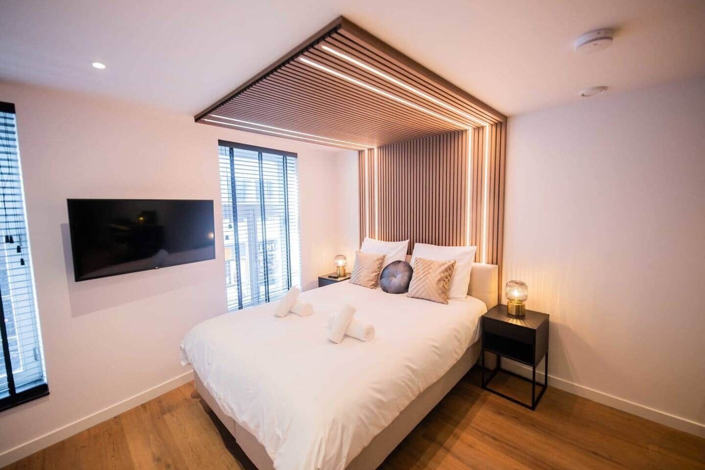 A modern bedroom with a large bed, a mounted TV, and a unique ceiling design.