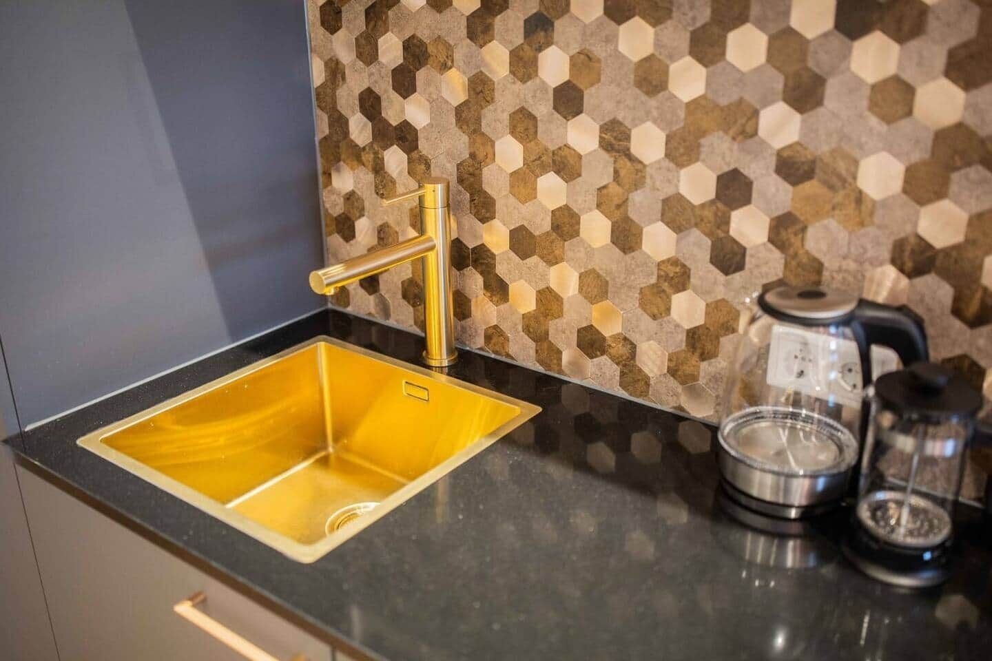 Et køkken med en gylden vask, kaffemaskine og en backsplash med et hexagonalt mønster.
